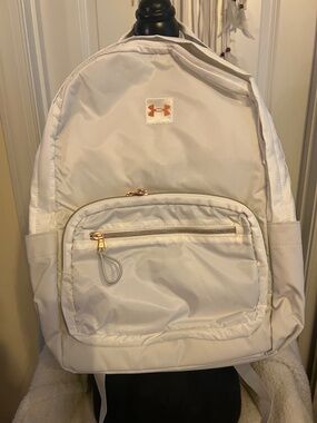 This is a Under Armour white and gold Studio Campus backpack.